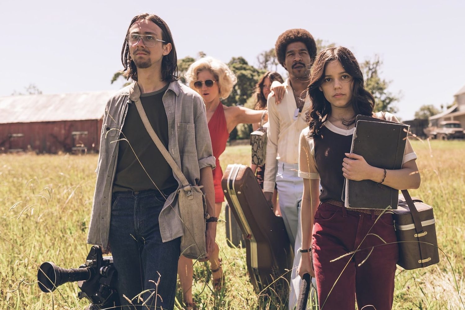 A group of people holding film equipment while walking in a field.