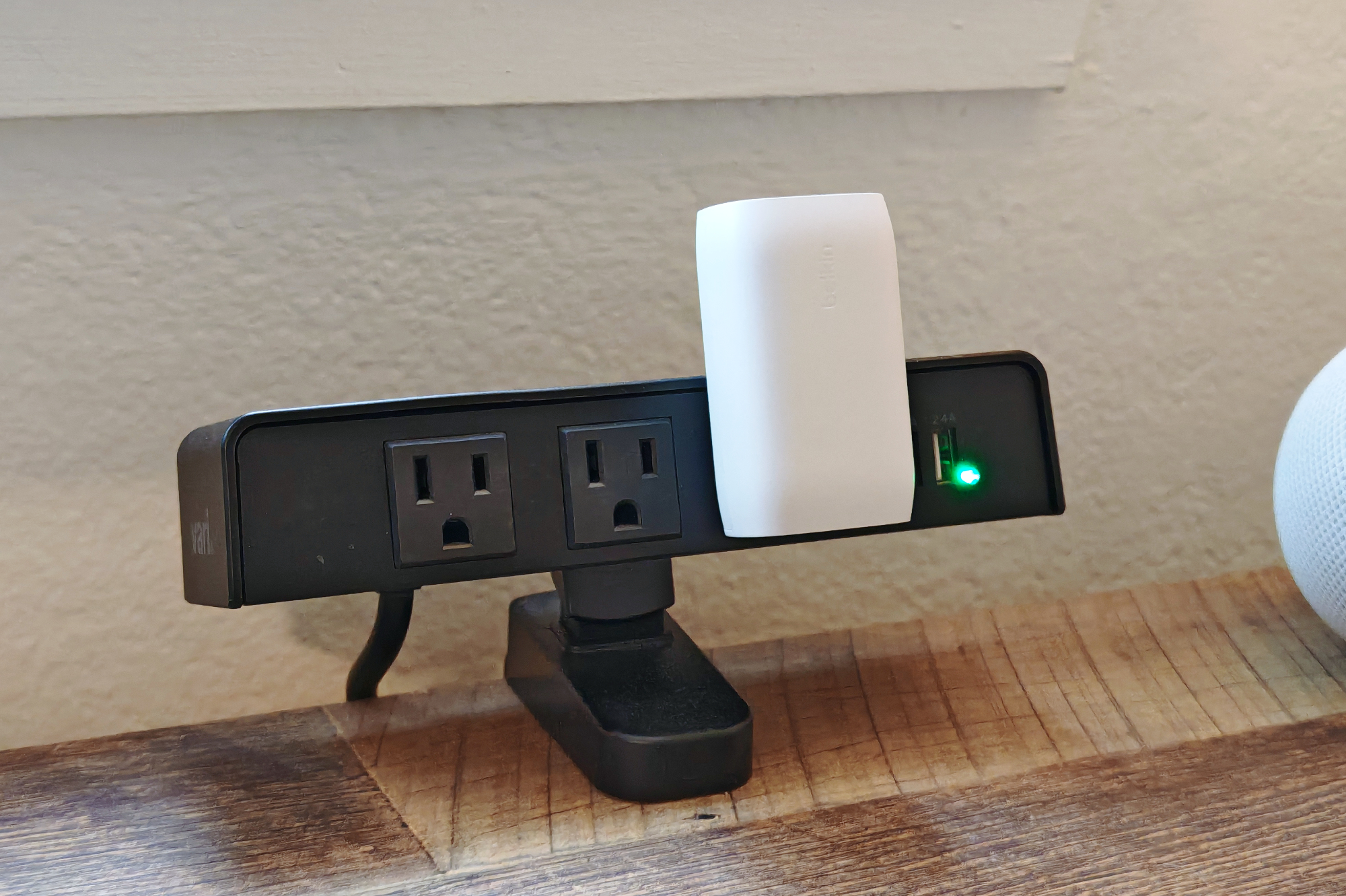 A white Belkin charger plugged into an outlet on a desk.
