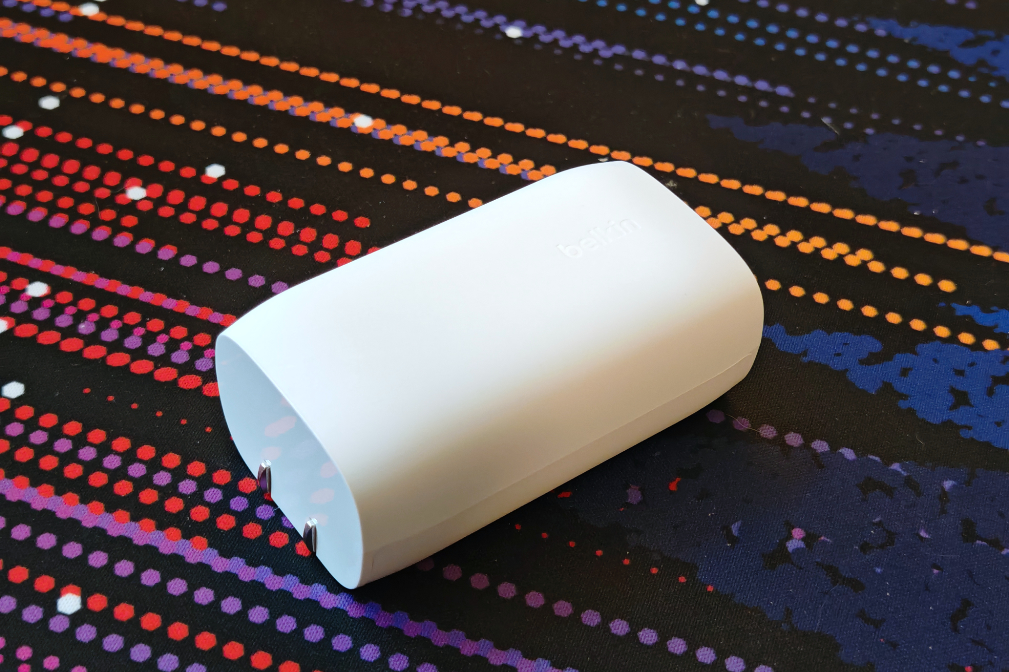 रंगीन डेस्क मैट पर एक सफेद बेल्किन चार्जर रखा हुआ है।