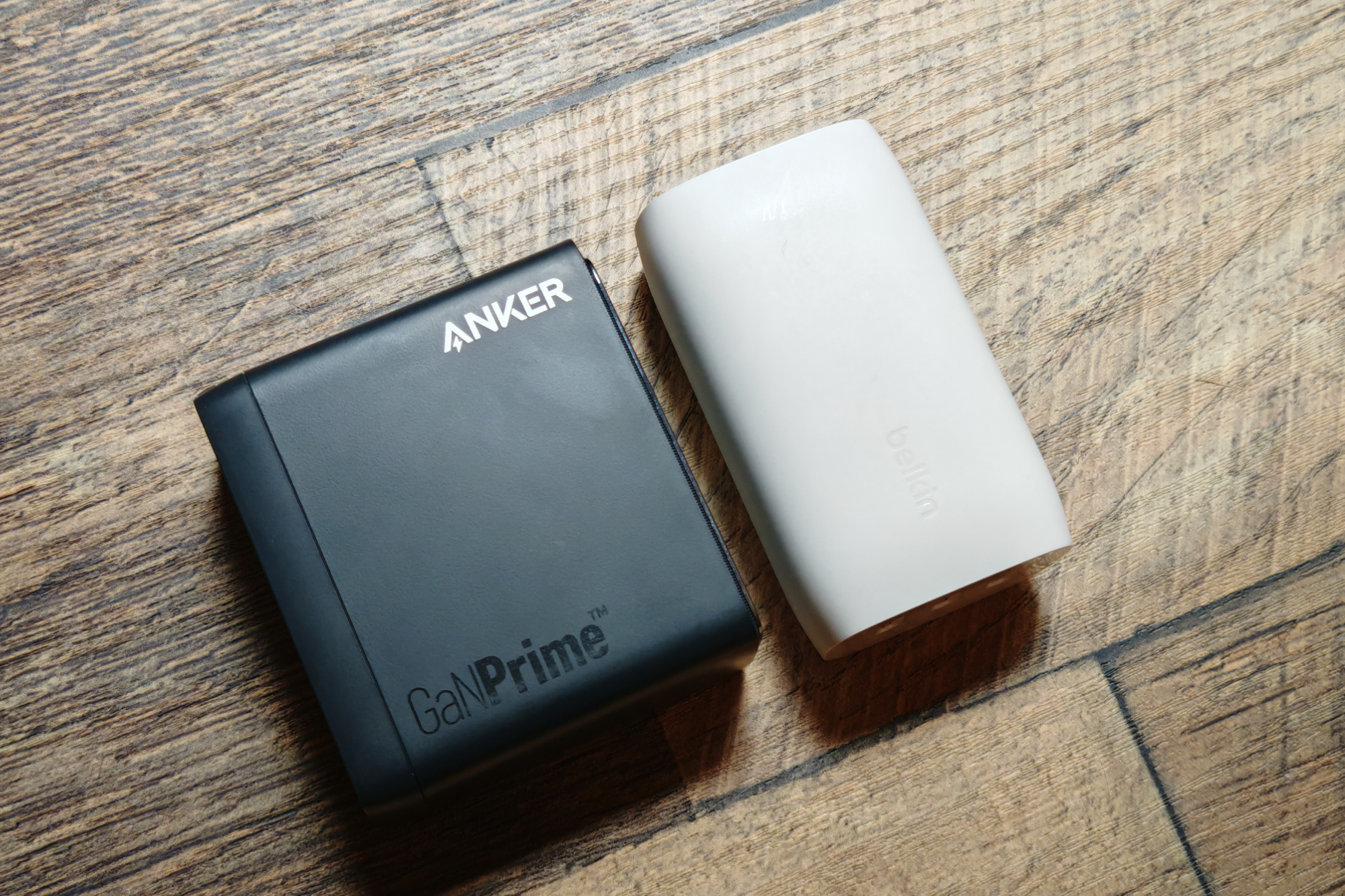 An Anker charger and a Belkin charger laying next to each other on a desk.