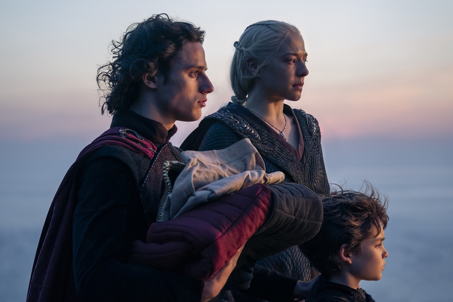 A woman stands with her two sons staring out to sea.