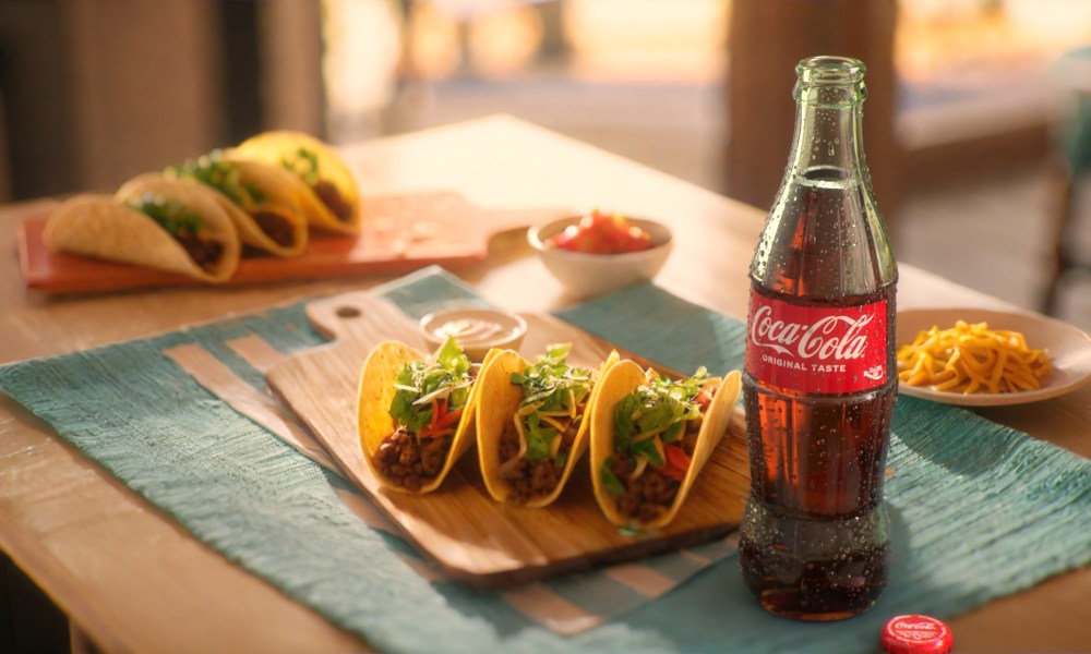 A glass of Coca-cola on a table next to some tacos