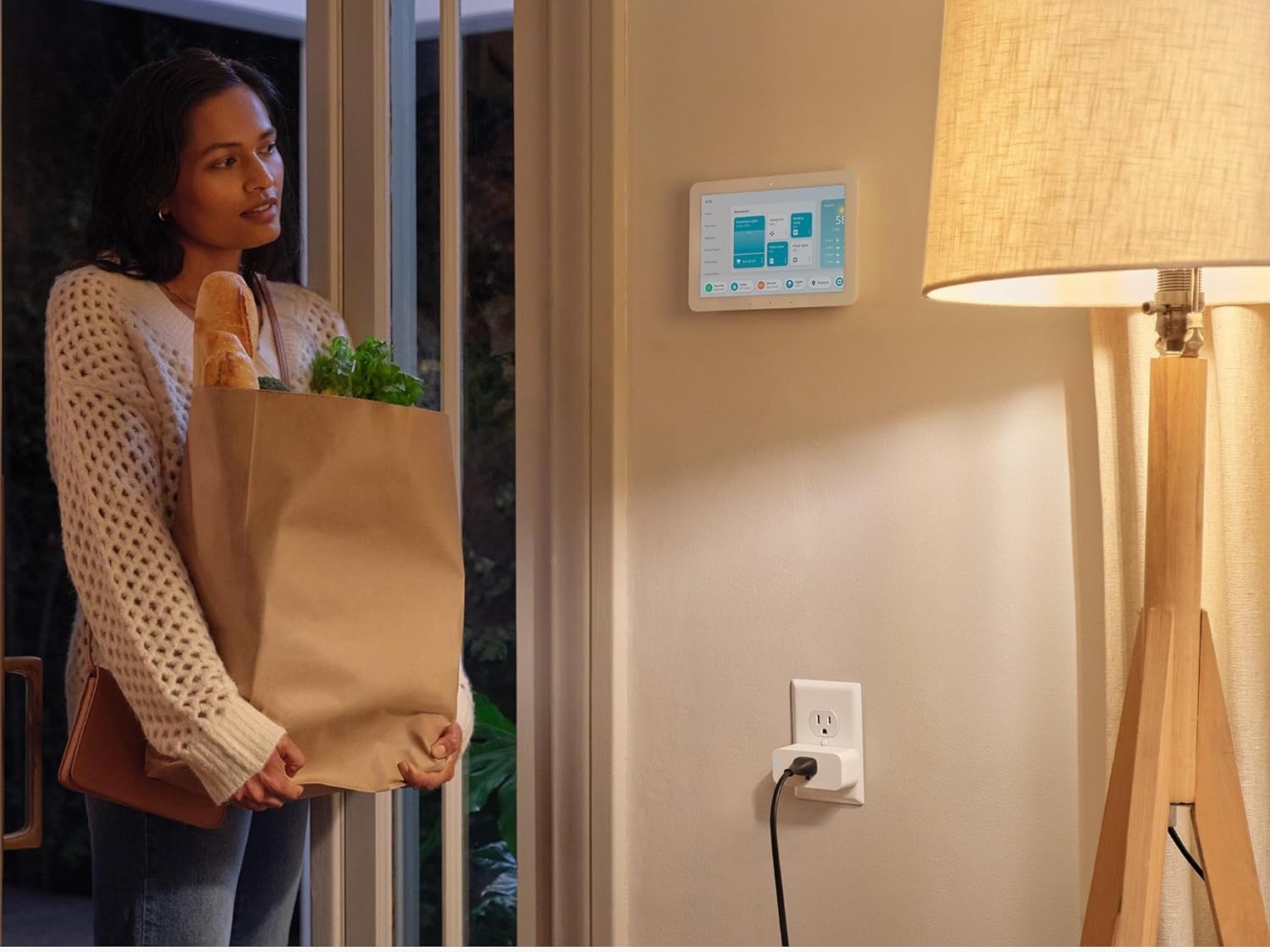 Una mujer parada en su casa cargando compras y mirando su Amazon Smart Plug.