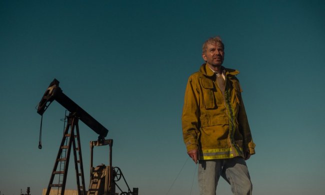 A man stands in front of an oil field and stares.