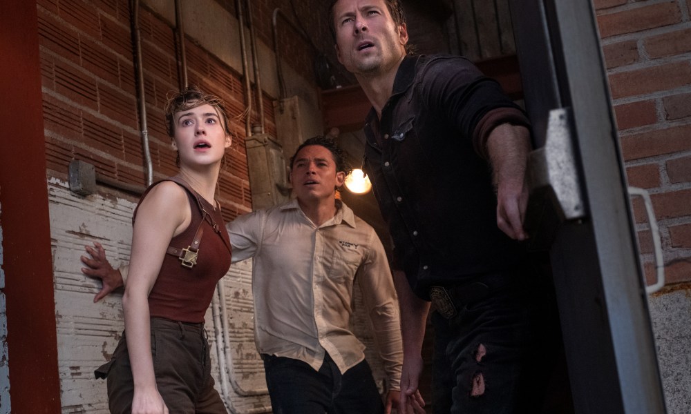 Daisy Edgar-Jones, Anthony Ramos, and Glen Powell look out an open doorway in fear in Twisters.