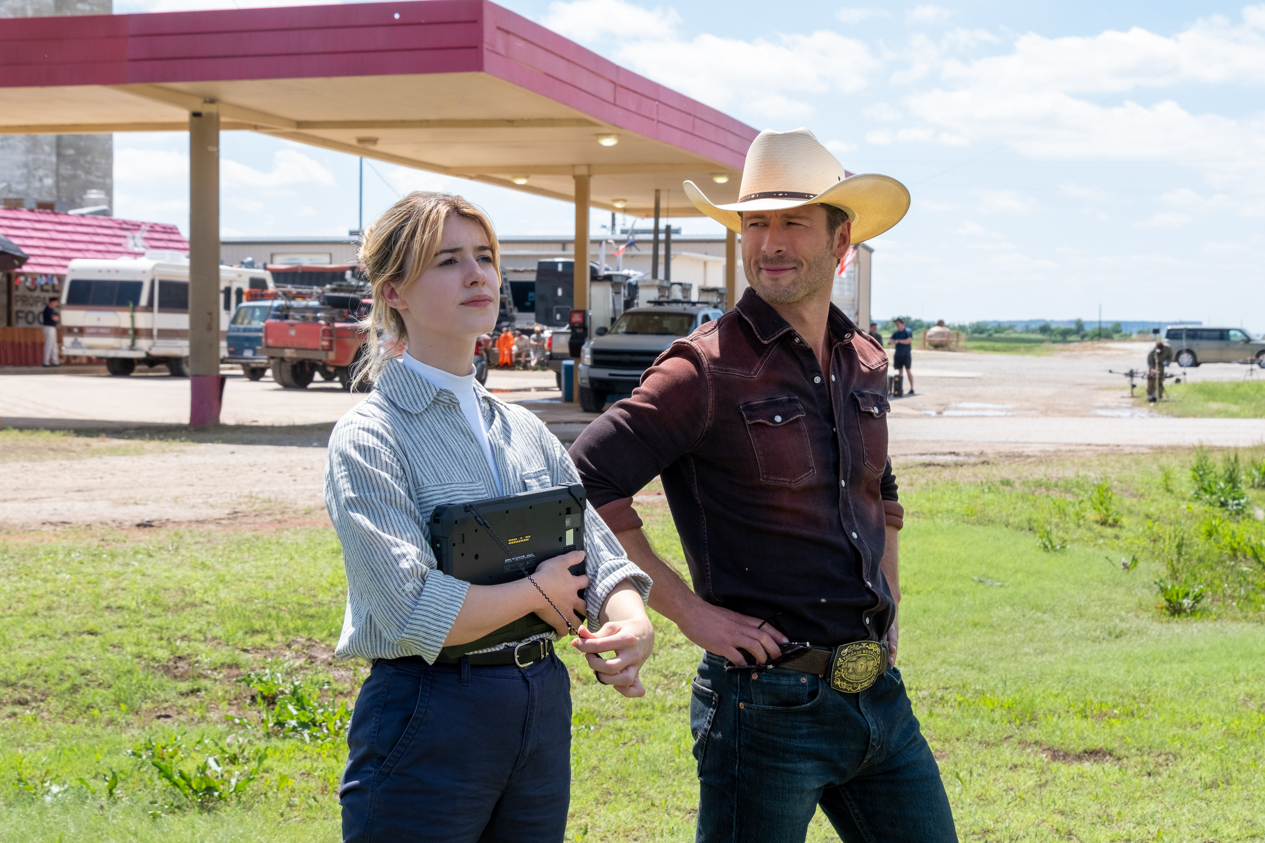 Daisy Edgar-Jones and Glen Powell stand near a gas station in Twisters.