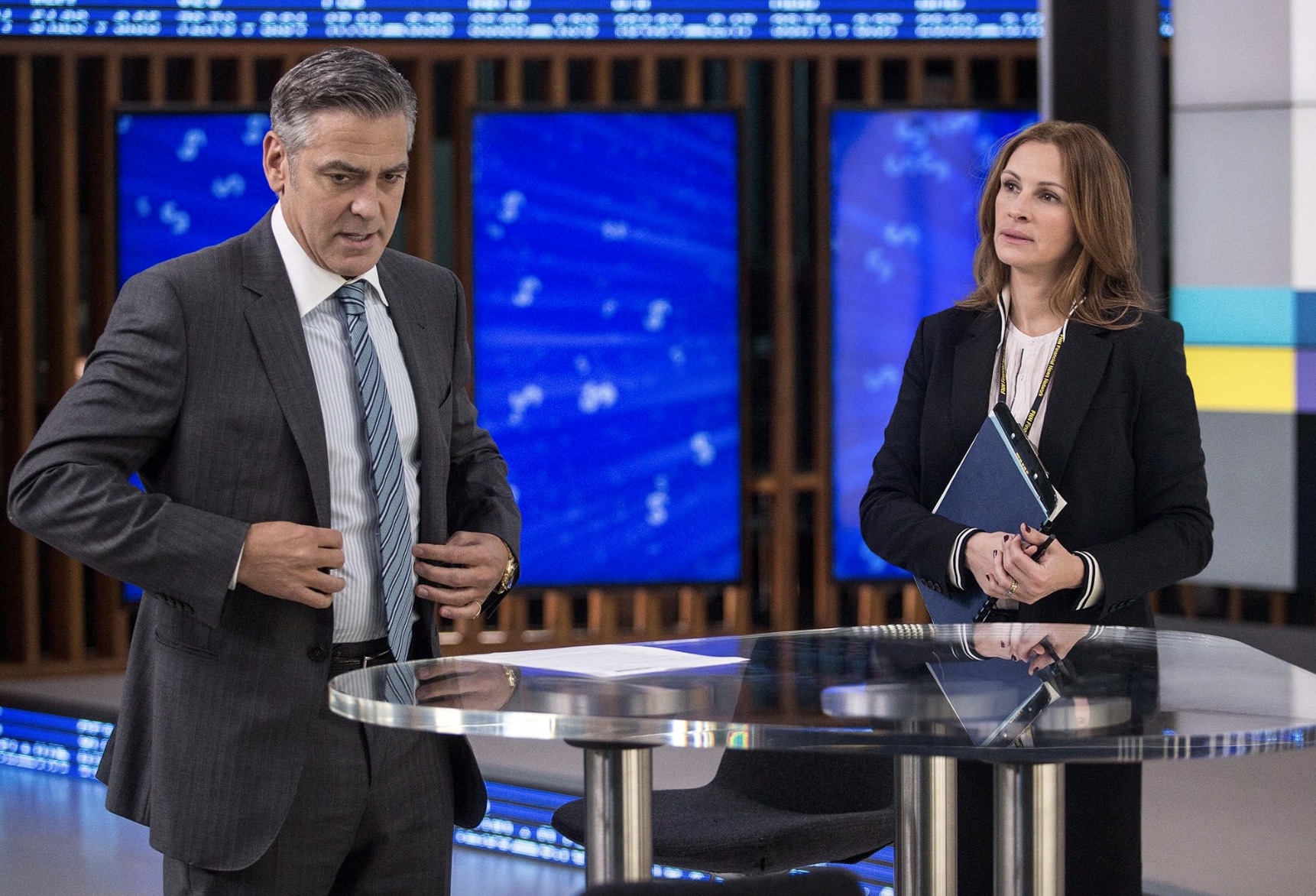 A man and woman stand in front of a desk and talk.