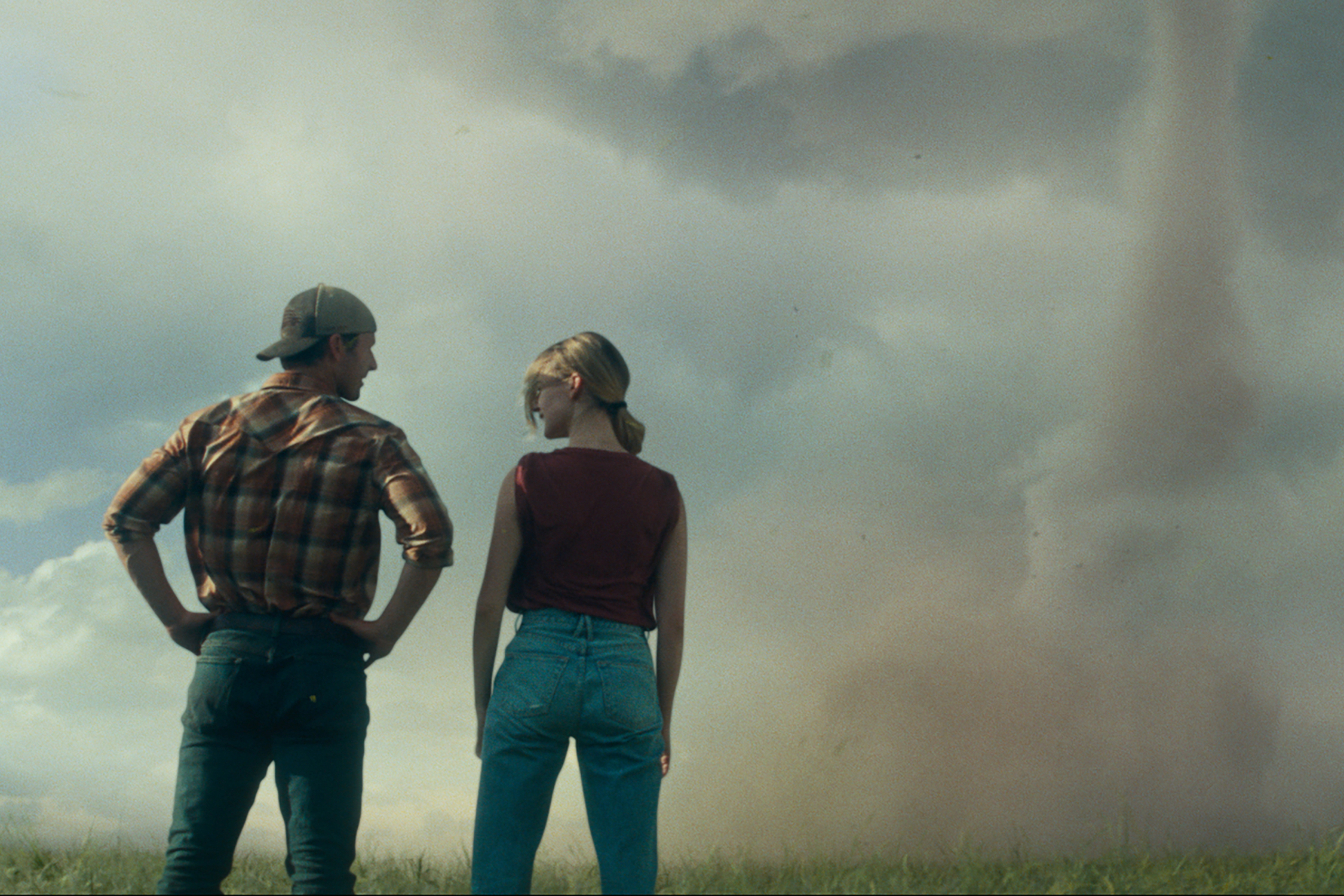 Glen Powell and Daisy Edgar-Jones stand in front of a tornado in Twisters.