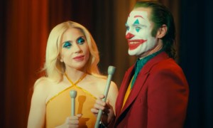 Lady Gaga and Joaquin Phoenix hold mics and smile in Joker 2.