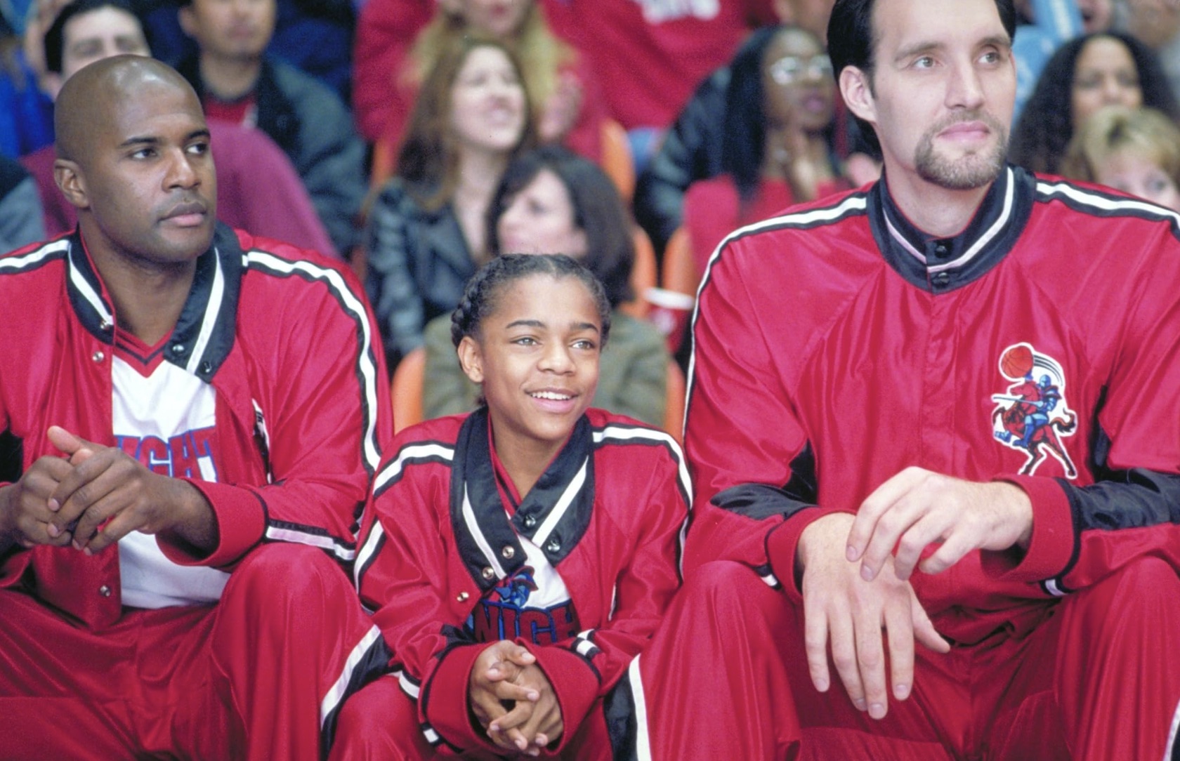 Un niño se sienta junto a dos jugadores de baloncesto en el banquillo.