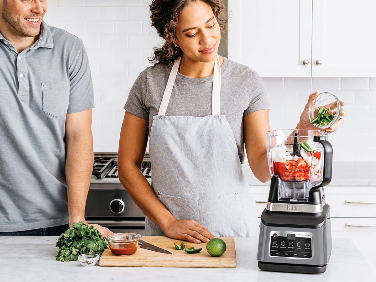 A woman pours food into the Ninja BN801 Professional Plus Kitchen System.