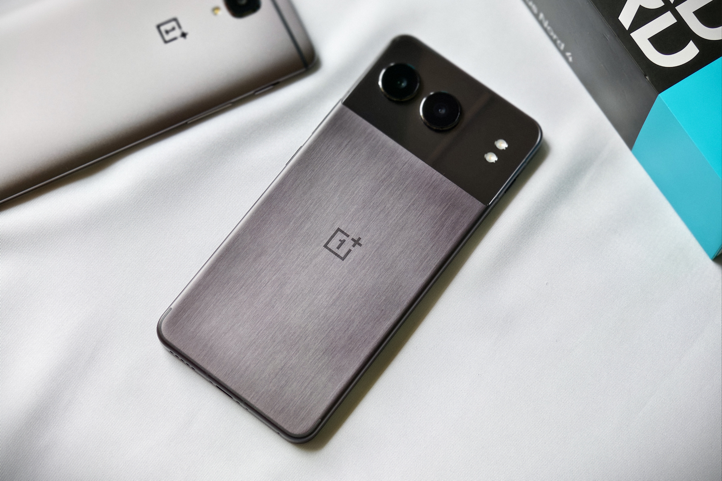 OnePlus Nord 4 na cor preta meia-noite com uma carcaça unibody de metal mantida em um tecido branco ao lado de um OnePlus 3T metálico.