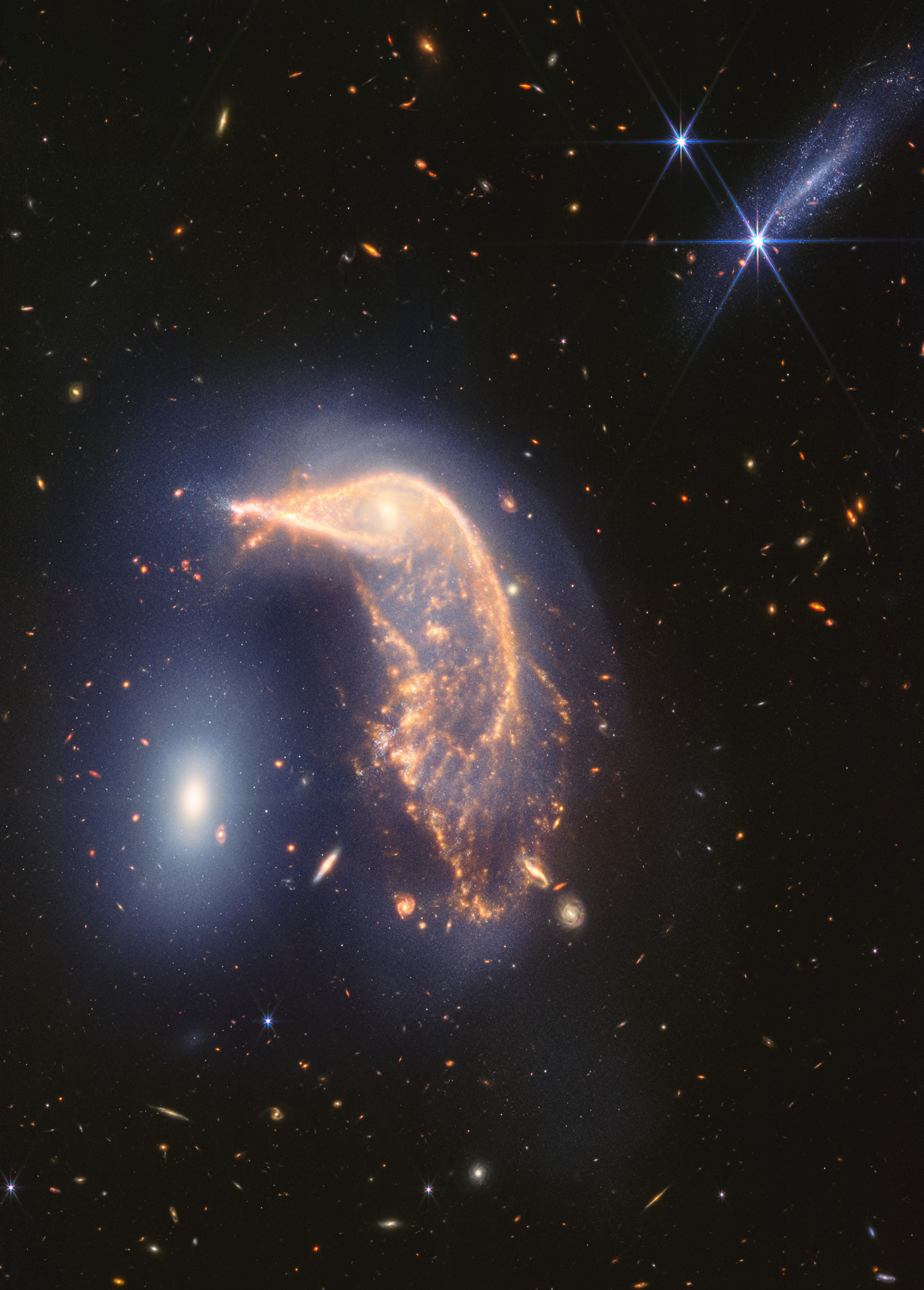 ¡Esta "fiesta de pingüinos" es ruidosa! La galaxia espiral distorsionada en el centro, el Pingüino, y la galaxia elíptica compacta a la izquierda, el Huevo, están encerrados en un abrazo activo. Una nueva imagen del infrarrojo cercano y medio del telescopio espacial James Webb, tomada para conmemorar su segundo año de ciencia, muestra que su interacción está marcada por un tenue resplandor azul en forma de U invertida.