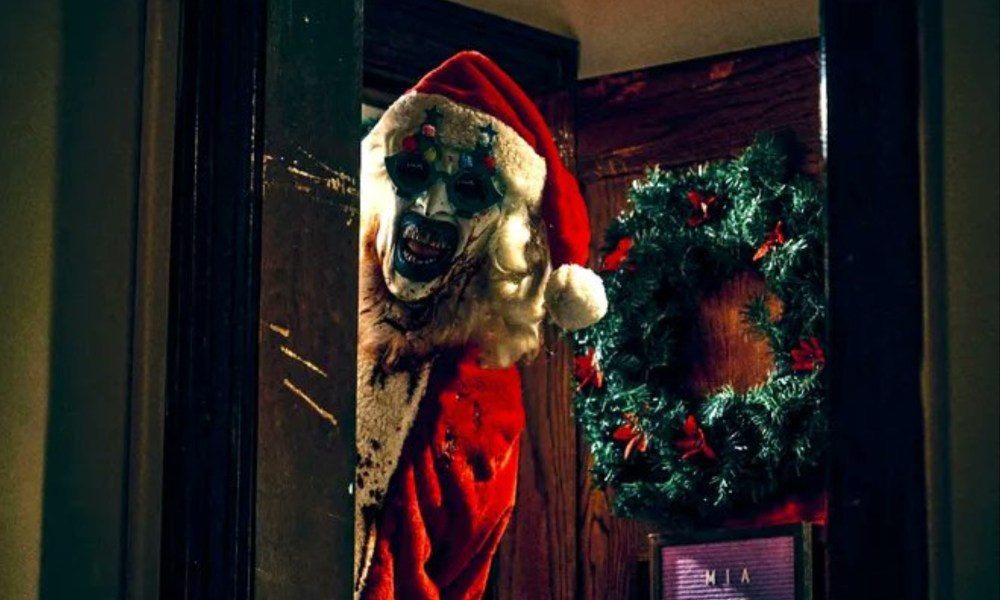 A bloody clown dressed like Santa Claus stands in the doorframe.