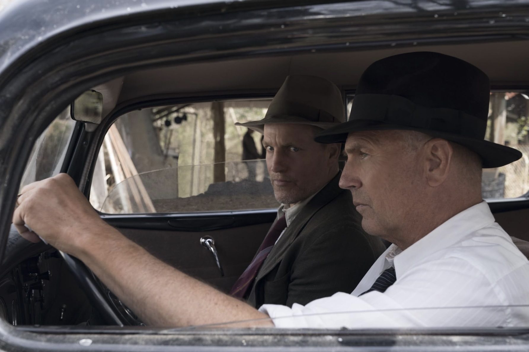 Kevin Costner se sienta al volante mientras Woody Harrelson observa desde el asiento delantero.