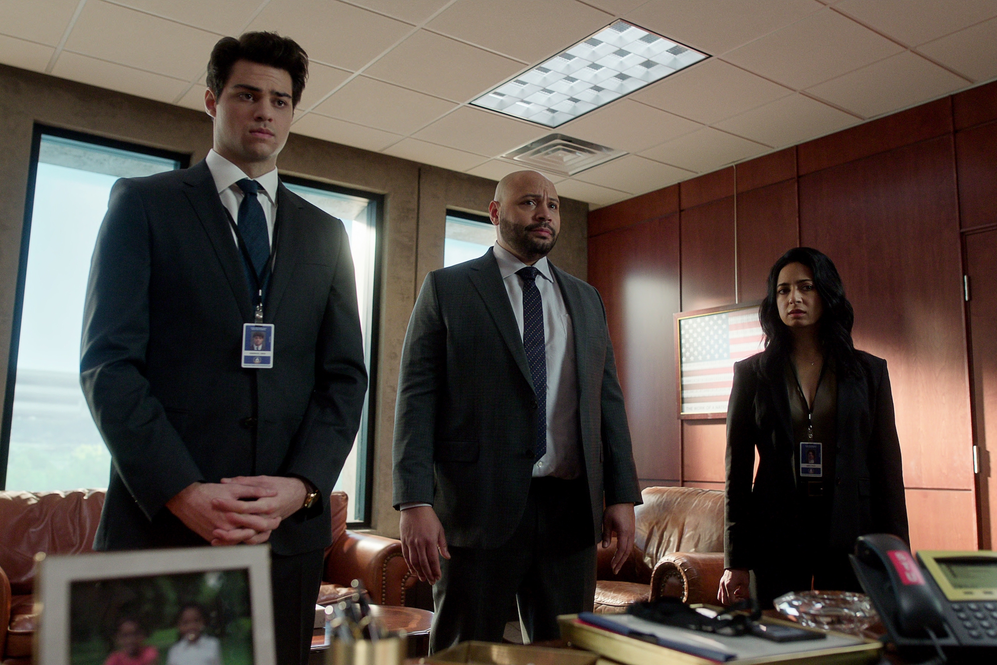 Three people stand patiently in front of a desk.