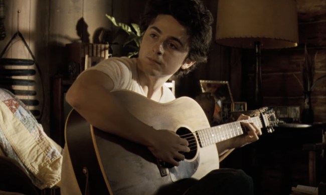 Timothee Chalamet holds a guitar and stares in A Complete Unknown.