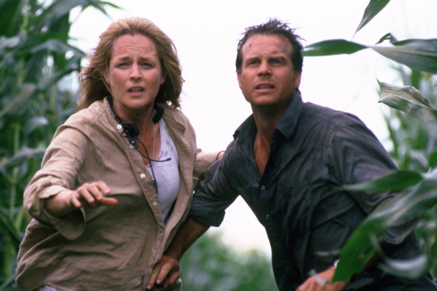 A woman and man look at a tornado while standing in a cornfield.