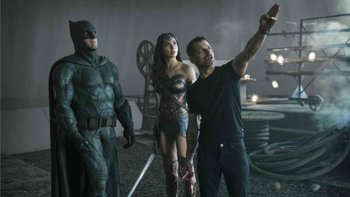 Zack Snyder puts his hand up and points in front of Batman and Wonder Woman.