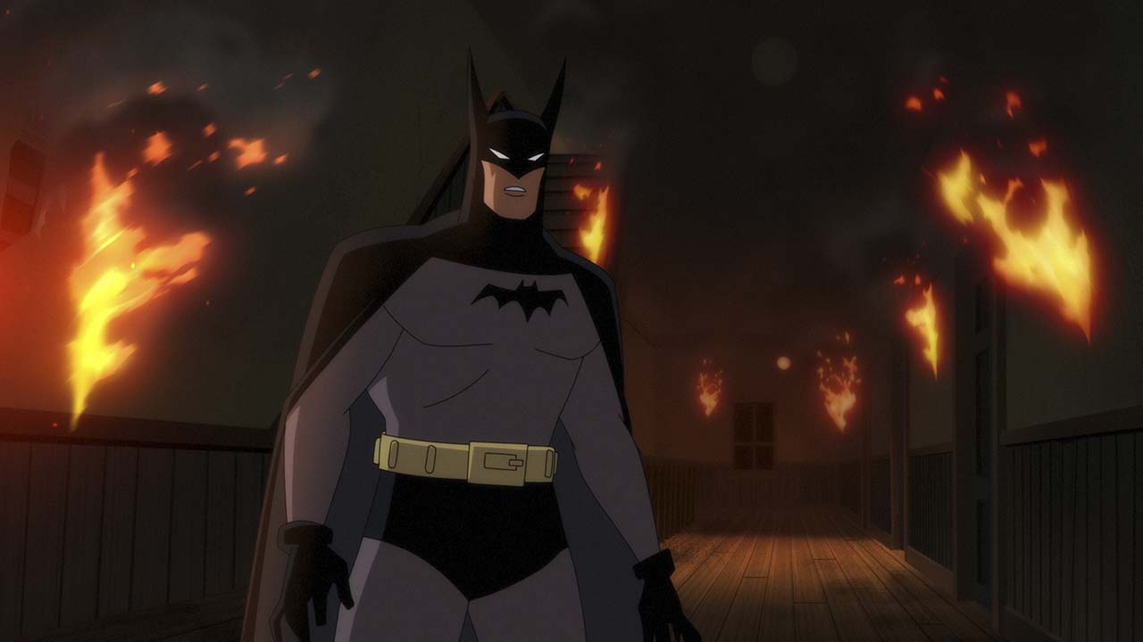 Un Batman animé avec une scène enflammée derrière lui dans Batman : Caped Crusaders