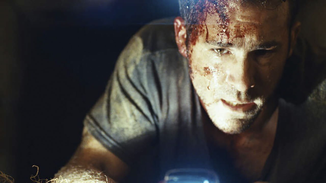 Ryan Reynolds in a dark coffin shining a light on his bloodied face in Buried.