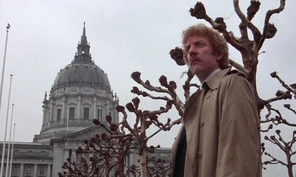 Un hombre se encuentra cerca de árboles desnudos en Invasion of the Body Snatchers.