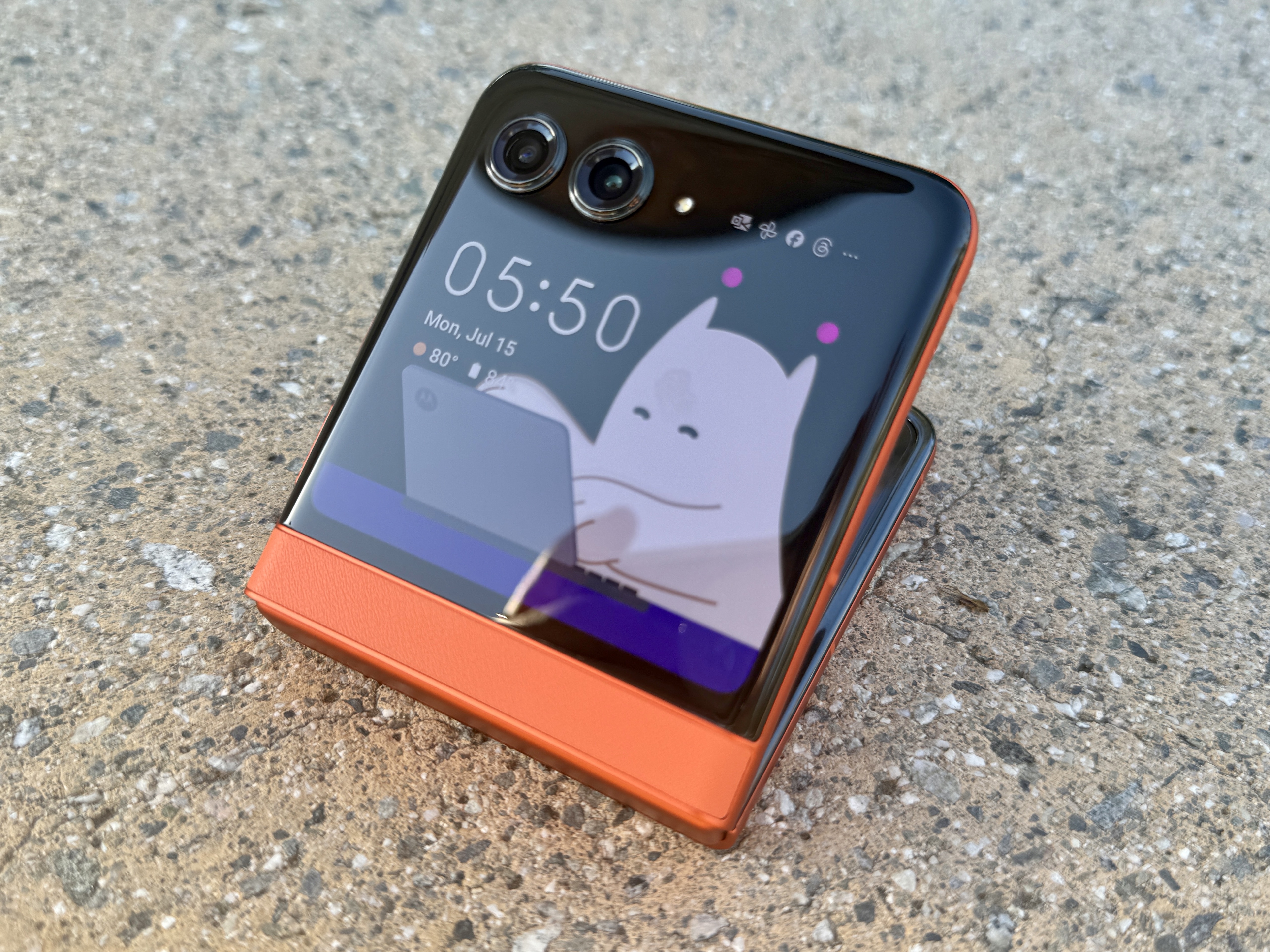 부분적으로 열린 커버 디스플레이에 Moo를 보여주는 Spritz Orange 색상의 Motorola Razr 2024.