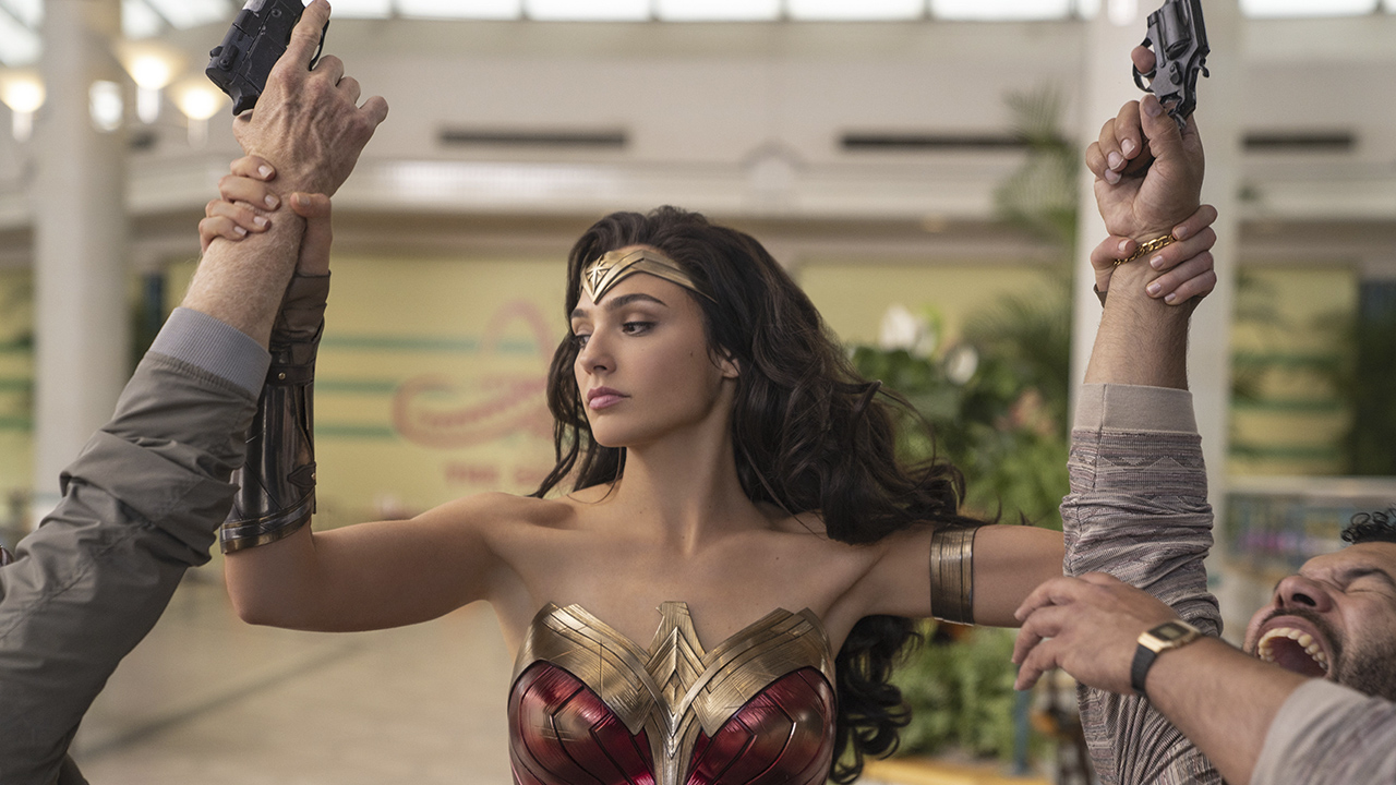 Gal Gadot as Wonder Woman holding two mens' arms that have guns in Wonder Woman 1984.