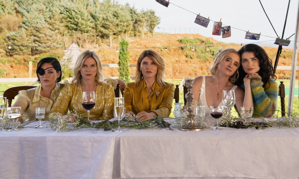 Five women sit at a table and stares.