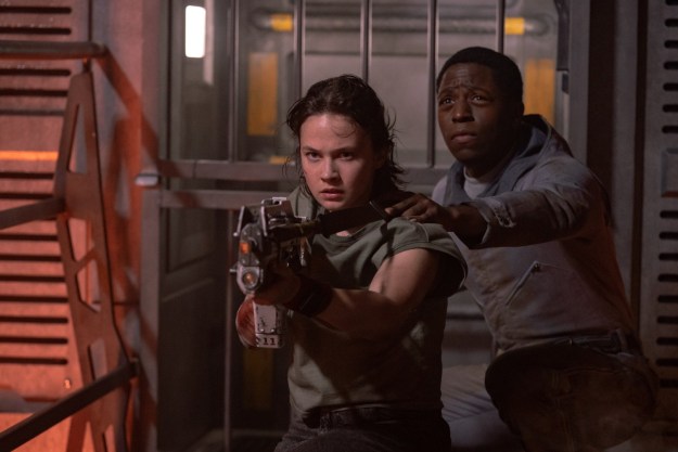 Cailee Spaeny aims a gun as David Jonsson stands behind her in a still from the movie Alien: Romulus.