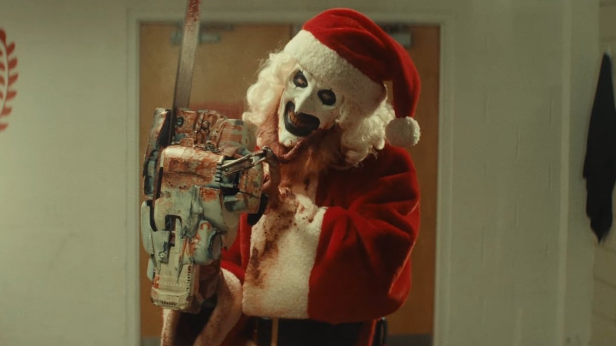 Art le clown habillé en Père Noël tient une tronçonneuse dans Terrifier 3.