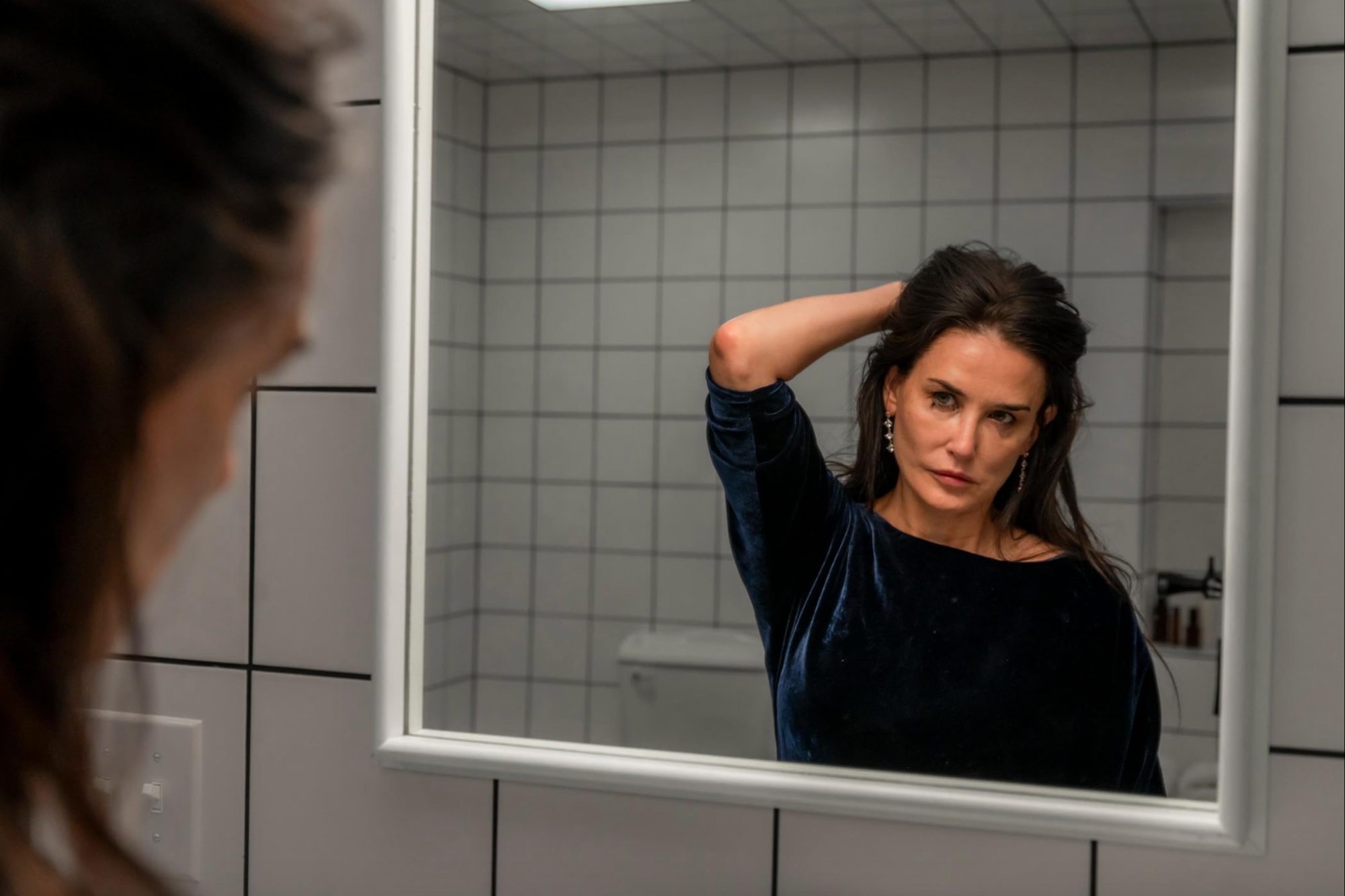 Demi Moore holds her hair back while staring in the mirror in "The Substance."