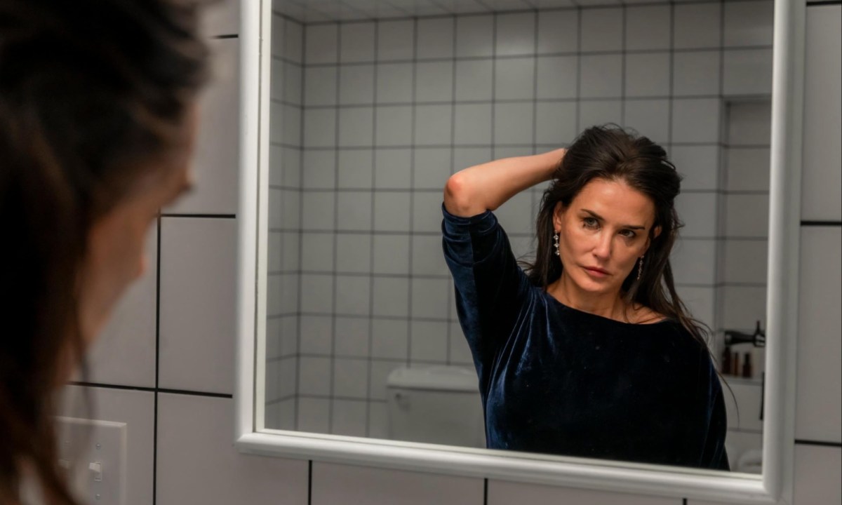 Demi Moore holds her hair back while staring in the mirror in "The Substance."