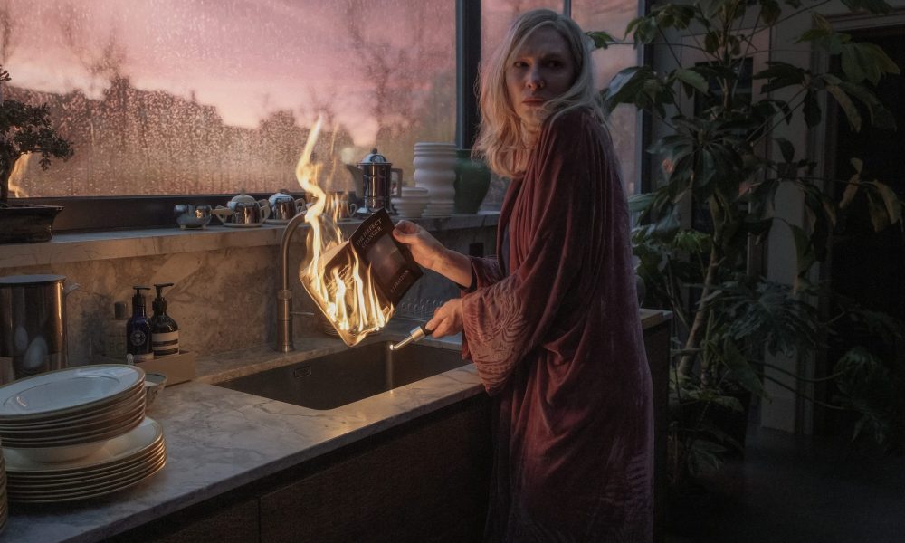 Cate Blanchett burns a book over a sink while staring behind her.