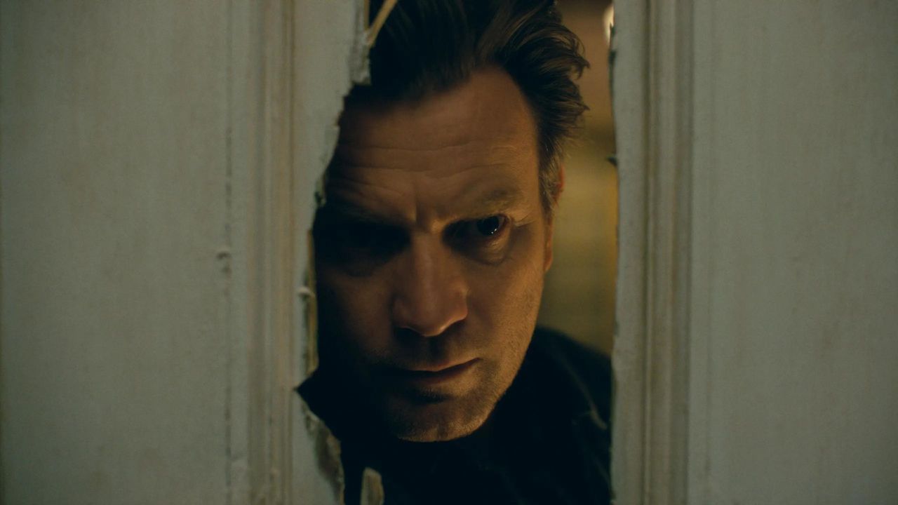 Ewan McGregor como Danny Torrance olhando através de um batente de porta quebrado em Doctor Sleep.