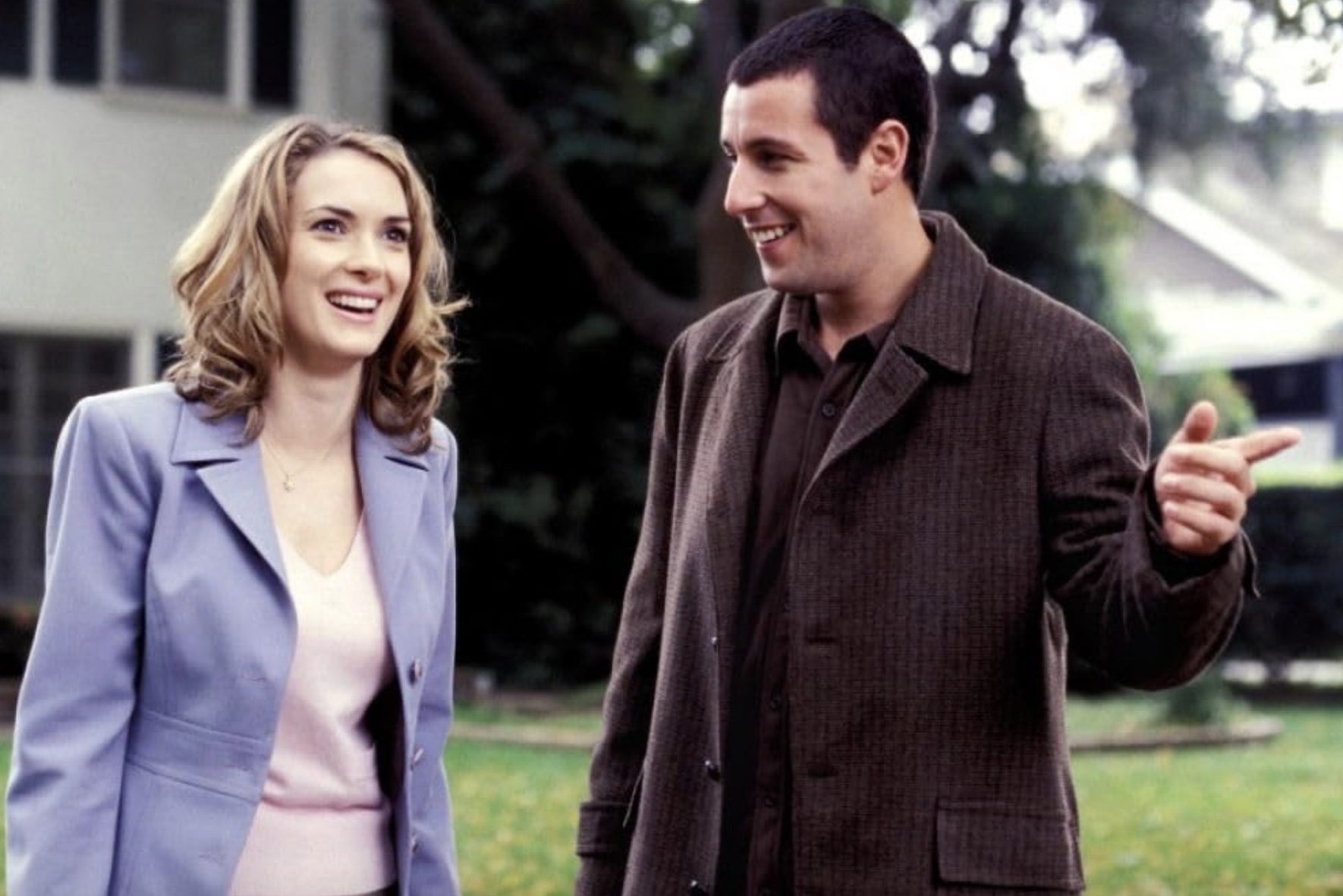 Adam Sandler señala y se para junto a una sonriente Winona Ryder.