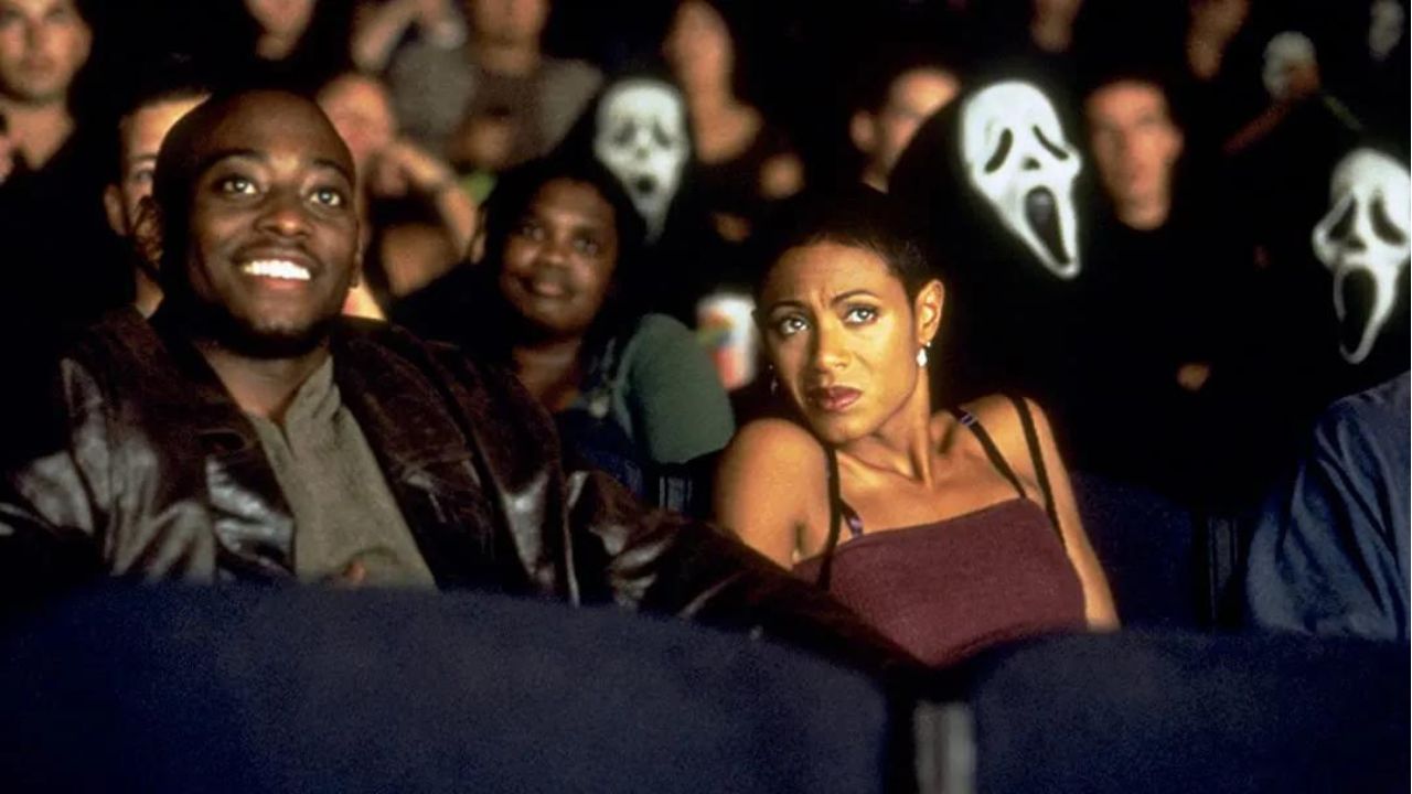 Omar Epps e Jada Pinkett como Phil e Maureen em um cinema cercado por pessoas com máscaras Ghostface em Pânico 2.