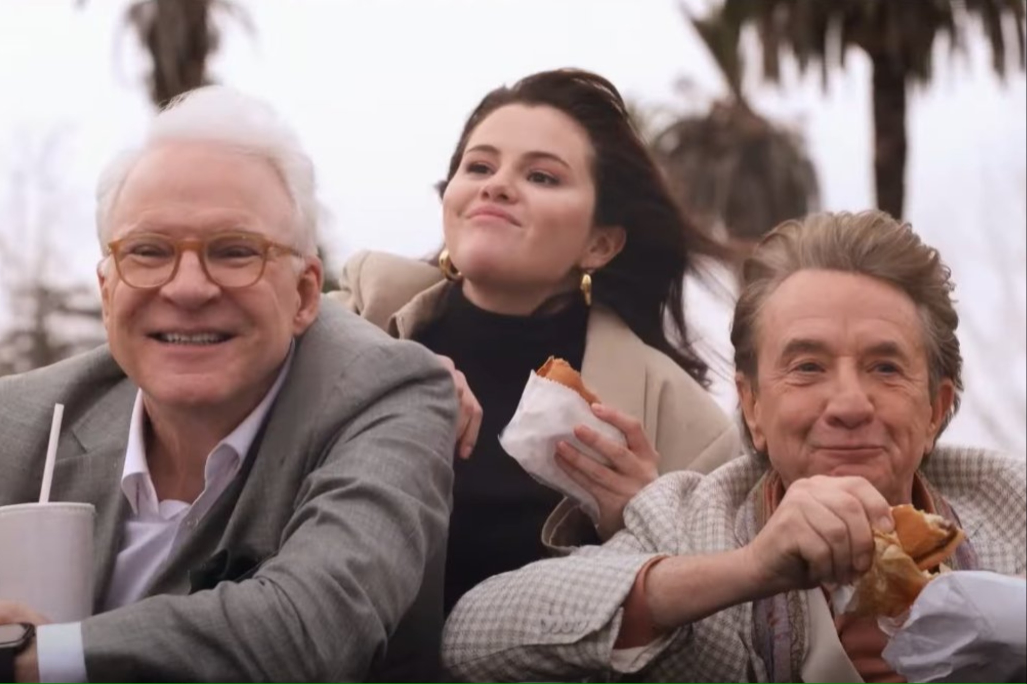 Two men and a woman stand out the roof of a car and eat.