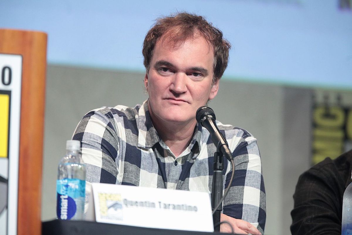 Quentin Tarantino est assis à une table avec un micro et regarde fixement.