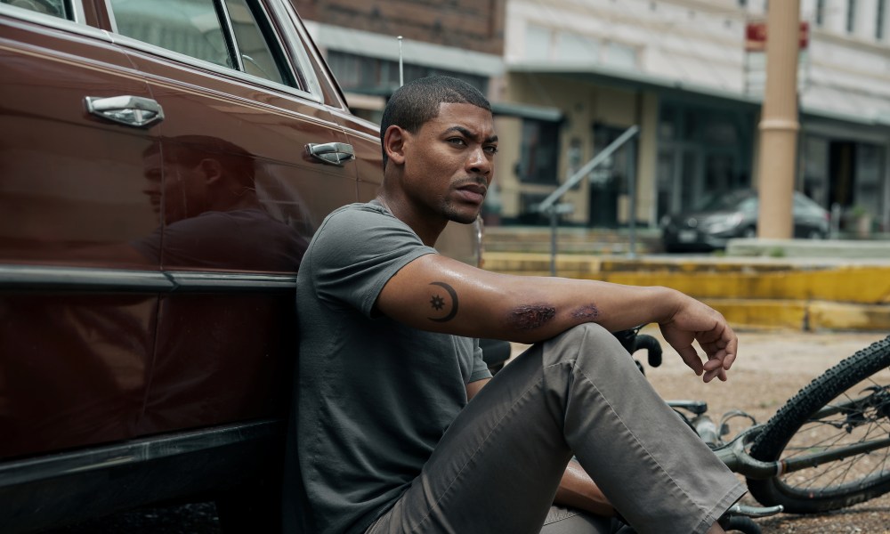 A man sits by a car in Rebel Ridge.