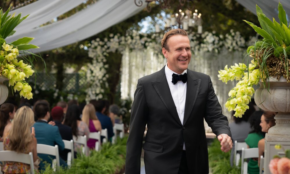 Jason Segel smiles and walks while wearing a tuxedo.