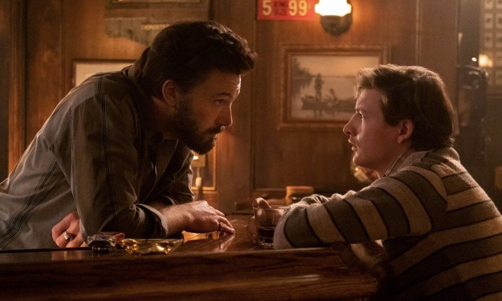 A bartender stands over his bar and looks at a customer sitting down.