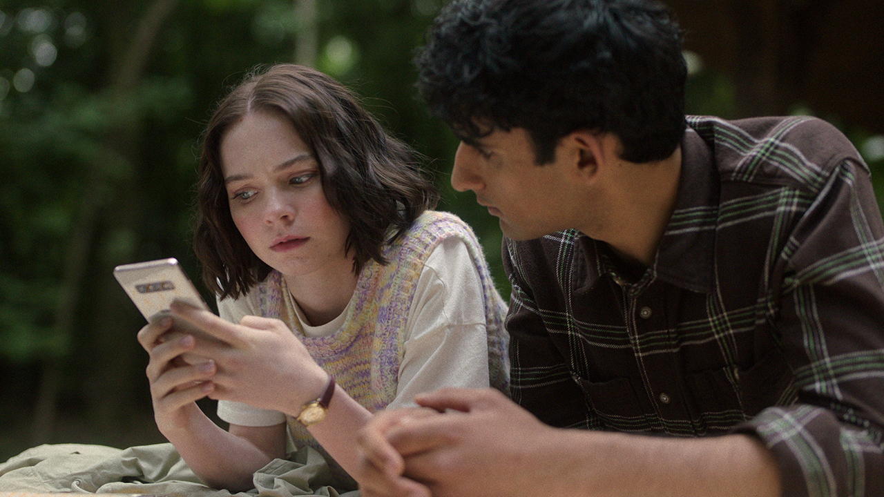 A young woman and man lean over a railing looking at her phone in A Good Girls' Guide to Murder.