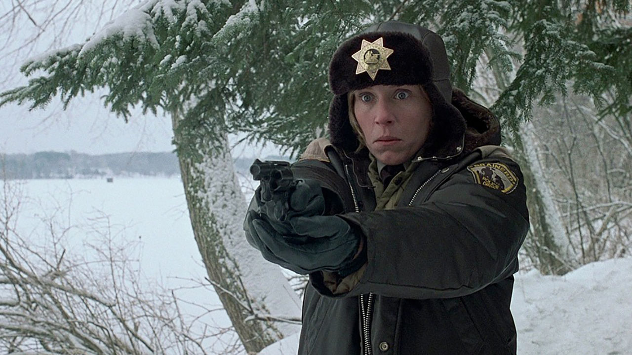 Frances McDormand in a police hat and uniform holding out a gun in the movie Fargo.