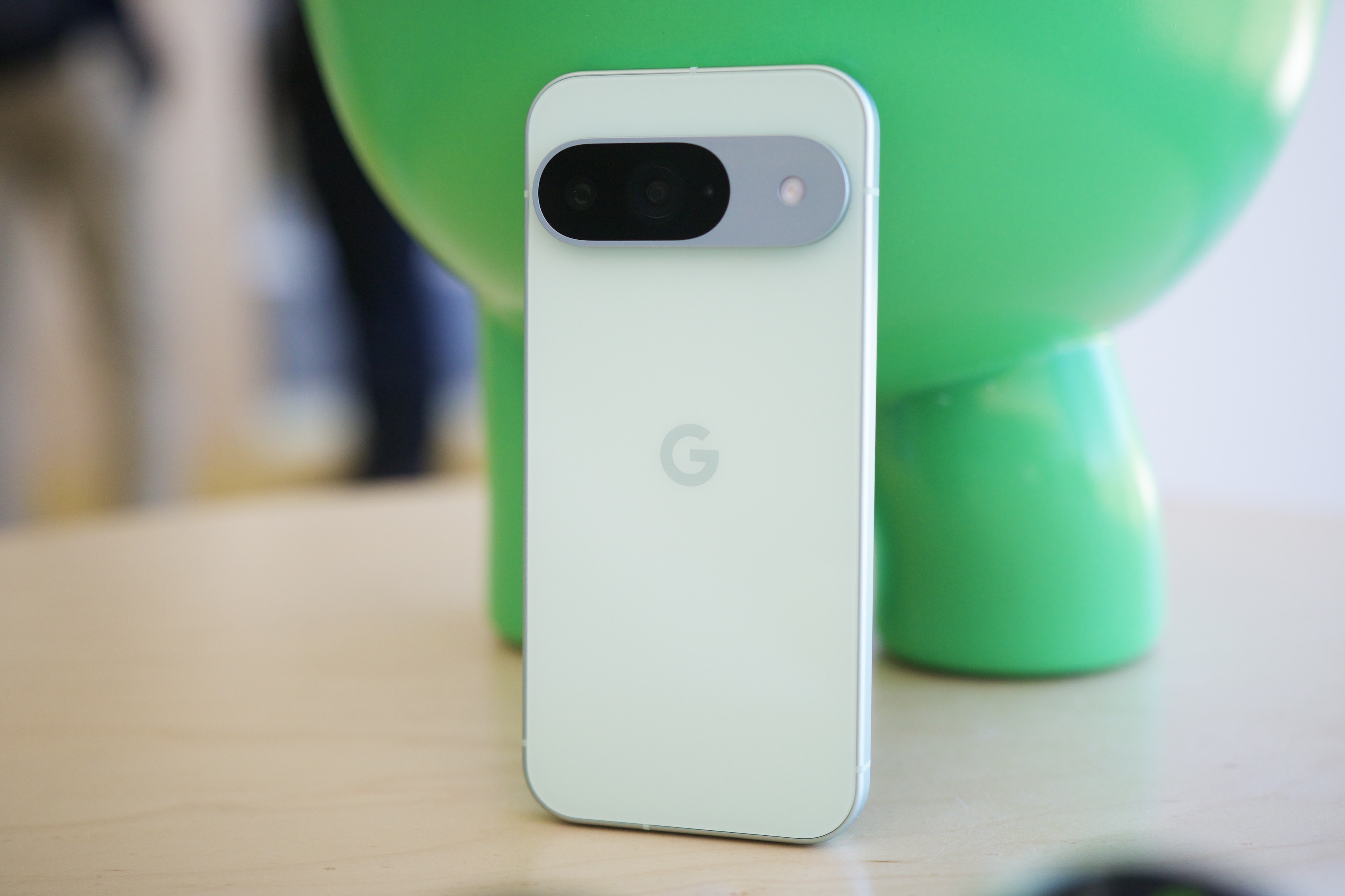 O Google Pixel 9 em pé ao lado de uma estátua do Android.