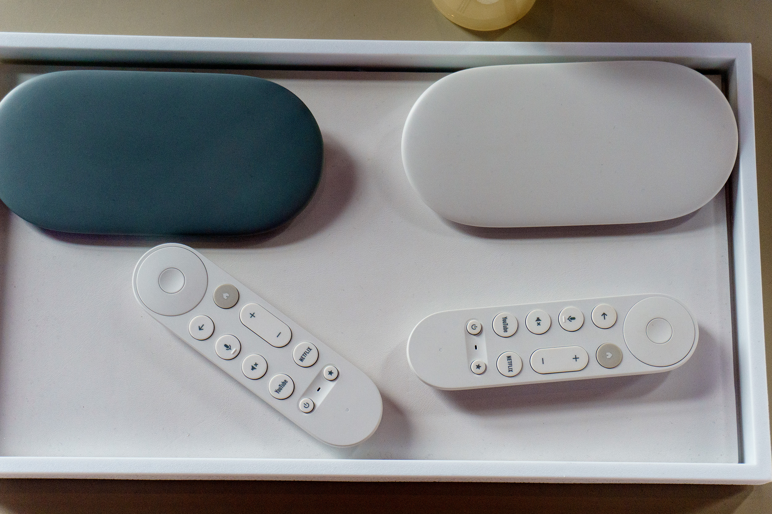 The two colors of Google TV Streamer — hazel and porcelain — with their remote controls.