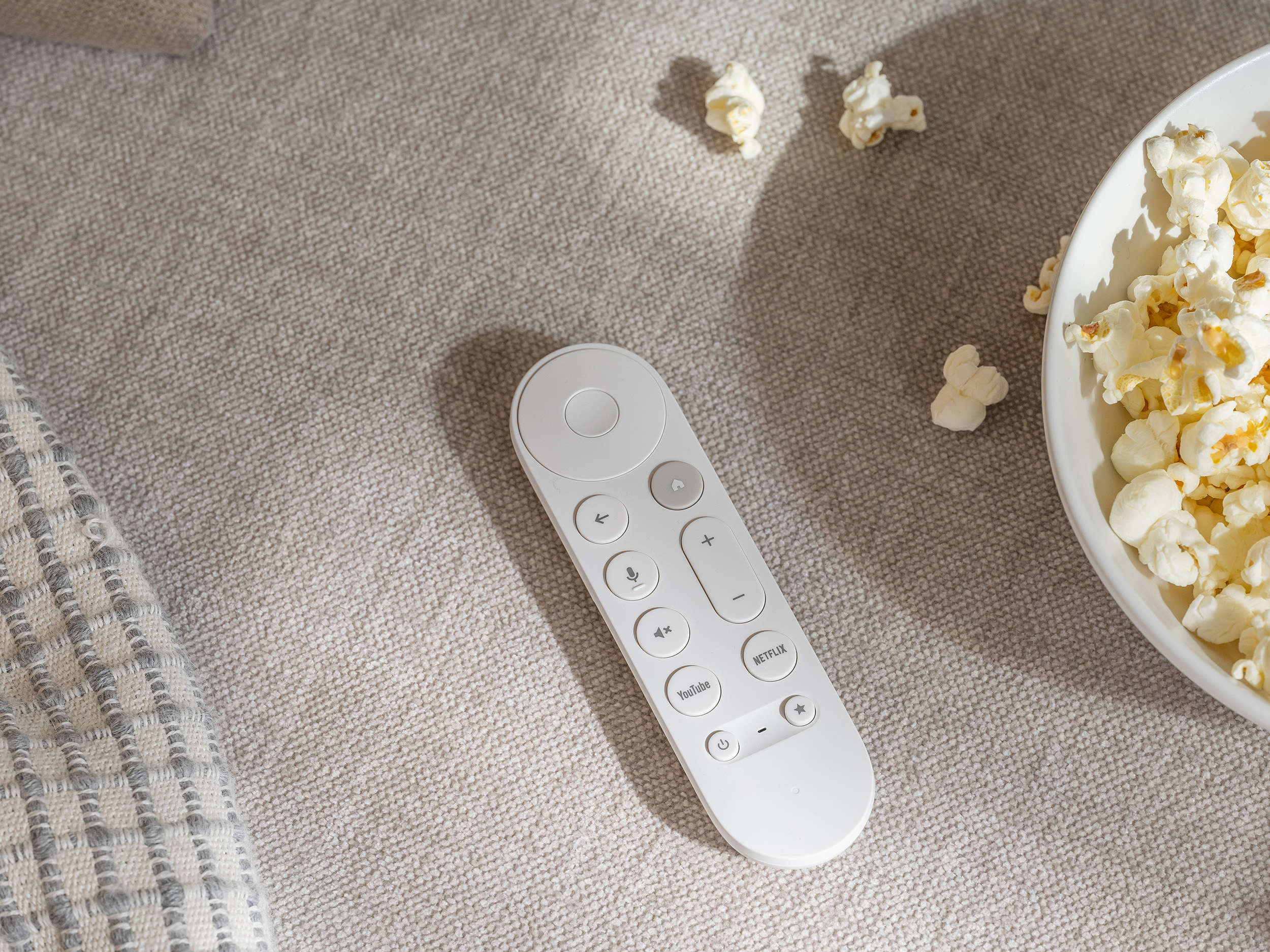 Une image promotionnelle de la télécommande Google TV Streamer à côté d'un bol de pop-corn.