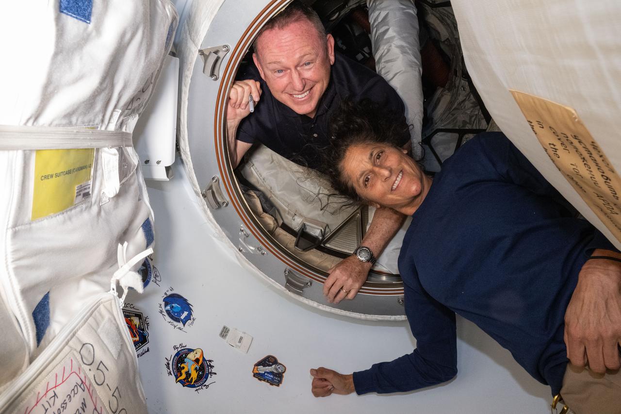 Os astronautas do Boeing Crew Flight Test da NASA (de cima) Butch Wilmore e Suni Williams posam em 13 de junho de 2024 para um retrato dentro do vestíbulo entre a porta dianteira do módulo Harmony da Estação Espacial Internacional e a espaçonave Starliner da Boeing.