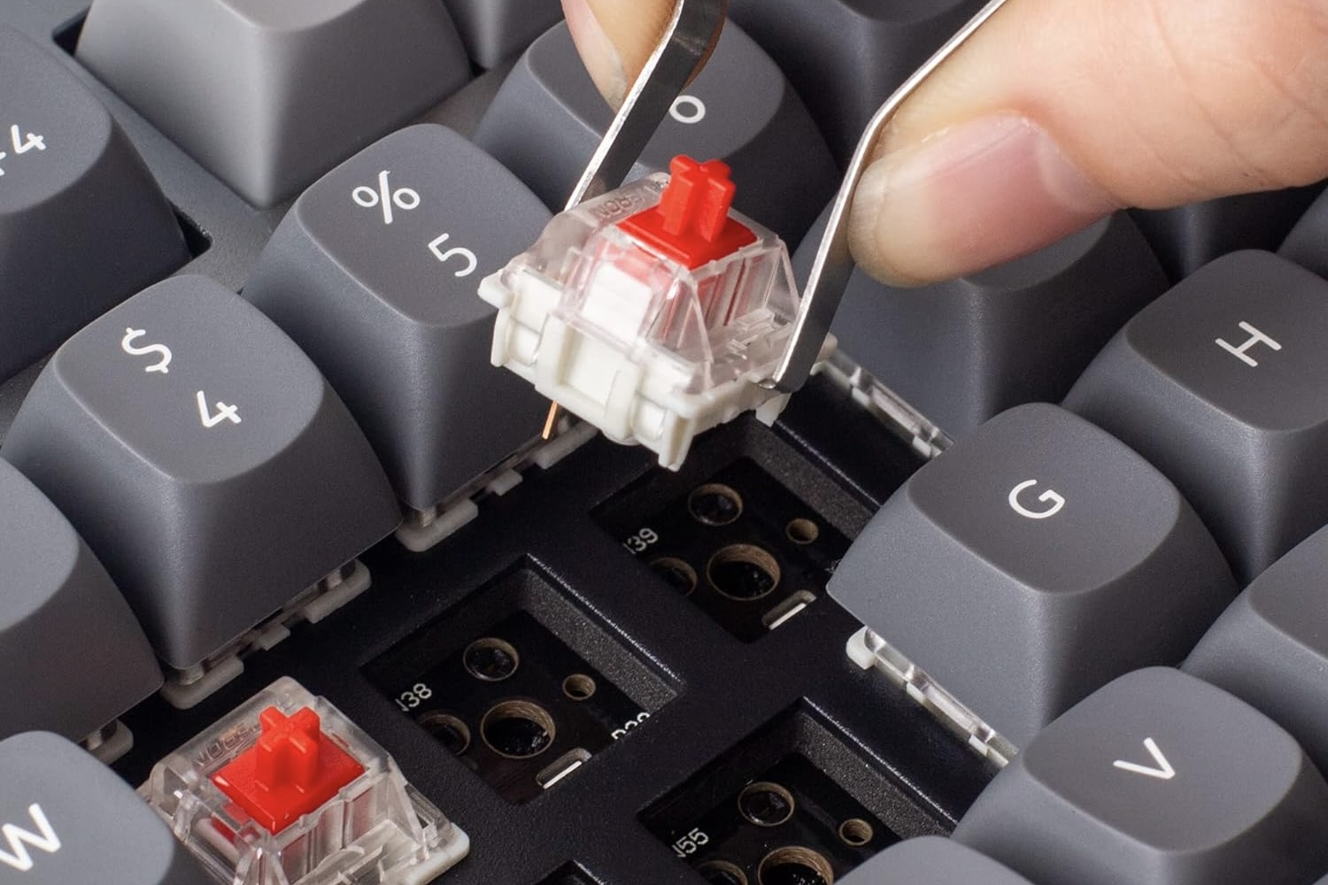 Una persona que usa unas pinzas para intercambiar teclas en el teclado mecánico Keychron Q3 QMK/VIA.