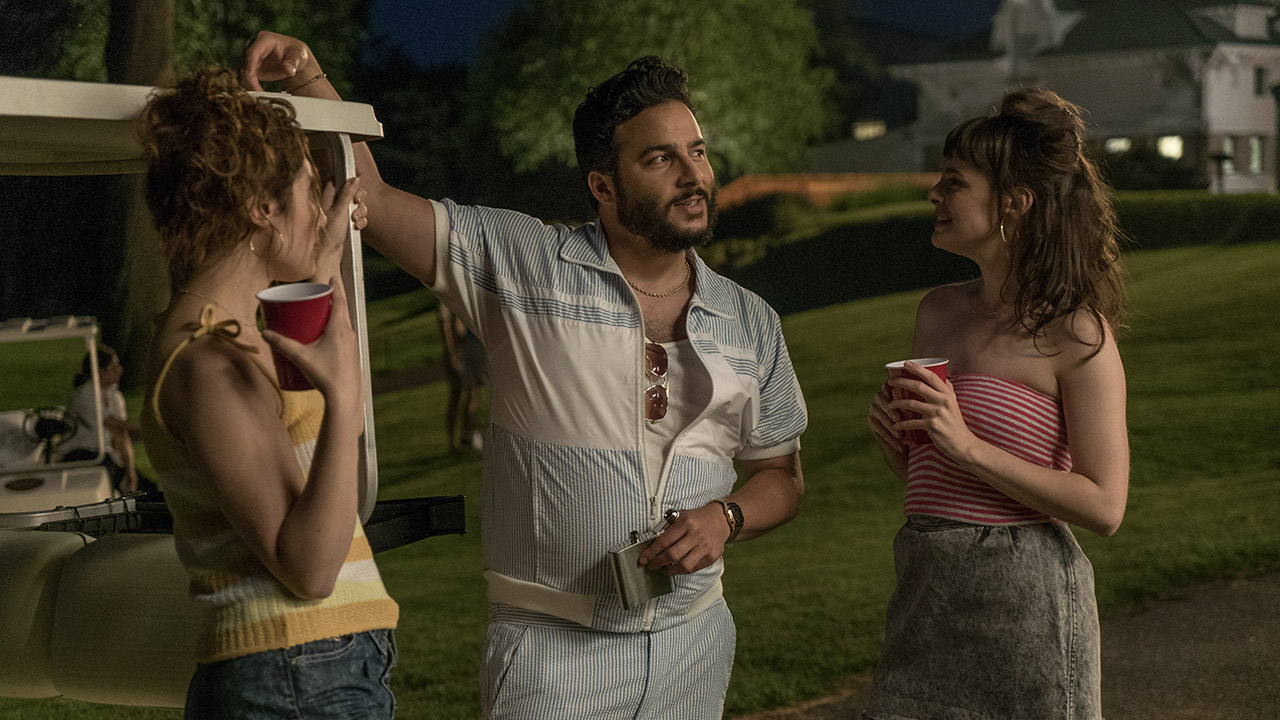 Um homem fica entre duas mulheres, tentando parecer legal em uma cena de Red Oaks no Amazon Prime Video.